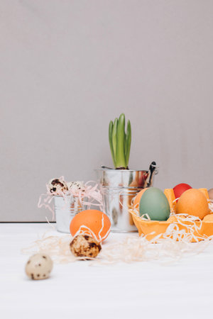 Painted multi-colored eggs in a yellow cardboard tray on a white wooden background. Easter...
