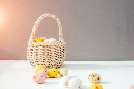 Colored eggs in a straw basket on a wooden white background. Symbol of the Easter holiday. Easter...