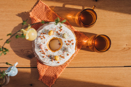 Round Easter cupcake decorated with white protein cream and colorful sprinkles and two mugs of tea on a wooden table in the kitchen. Top viewの写真素材