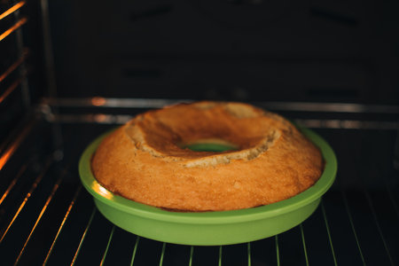 Baked round cake in a green silicone mold in the oven. Cooking desserts at home. Front viewの写真素材