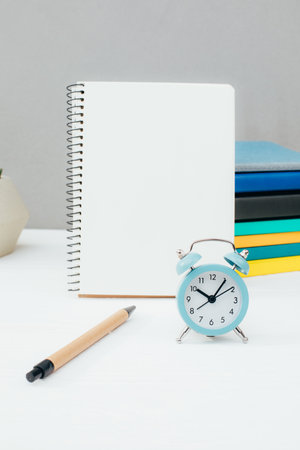 Workplace with stationery. Multicolored notepads, blue alarm clock, succulent on a white wooden table against a gray wall. Front viewの写真素材