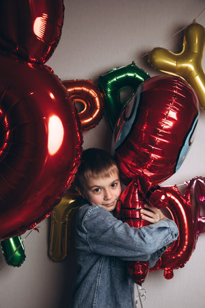 Childrens birthday celebration. A joyful boy, a schoolboy, in a blue shirt against the background of colorful balloons. Front viewの写真素材