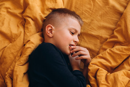 The boy lies in a yellow bed and grimaces from pain or untidiness. View from aboveの写真素材