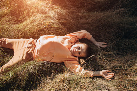 A joyful boy lies in tall grass in a meadow. Outdoor leisure in the park. Top view