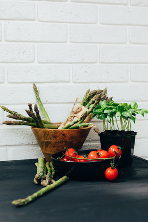 Healthy food background. A fresh vegetables, asparagus in wooden plate, tomatoes in black plate and green basilica on white wooden background. Flat layの写真素材