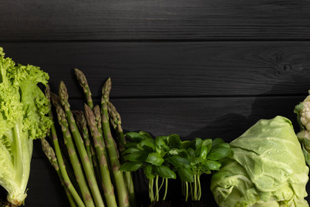 Set of green fresh vegetables, asparagus, cabbage, cauliflower, green salad, basilica on black wooden background. Flat layの写真素材