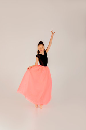 Ballet concept. A girl in a black gymnastic leotard in a beautiful graceful pose on a white background in pointe shoes and a pink skirt. Front viewの写真素材