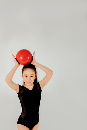 A girl gymnast in a black leotard with a red ball on a white background, close-up portrait. Front viewの写真素材