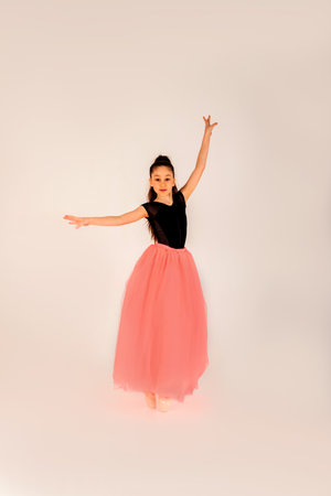 Ballet concept. A girl in a black gymnastic leotard in a beautiful graceful pose on a white background in pointe shoes and a pink skirt. Front viewの写真素材