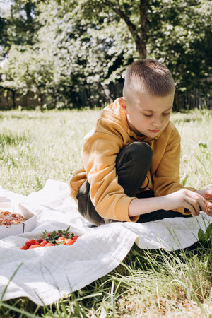 Family picnic. A boy in a green garden in sunny weather on a picnic eating pizza. Front viewの写真素材