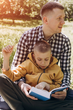 Family picnic. Dad and son in a green garden in sunny weather on a picnic eating pizza and reading book. Front viewの写真素材