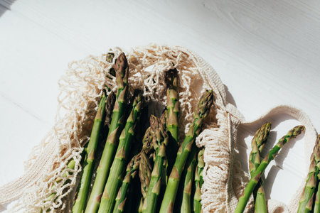 Healthy food background. A fresh asparagus on white wooden background in mesh bag. Top view
