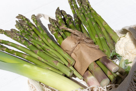 Healthy food background. A fresh asparagus on white wooden background in mesh bag. Top view