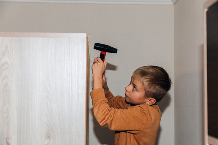 Close-up boy with a hammer driving nails on the back wall of furniture. Front view, selective focusの写真素材