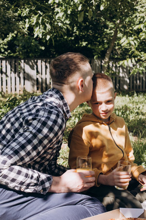 Family picnic. Dad and son in a green garden in sunny weather on a picnic eating pizza and drinking juice. Front viewの写真素材