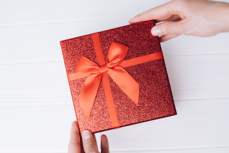 Shiny holiday red gift in female hands on a white wooden background. Flat layの写真素材