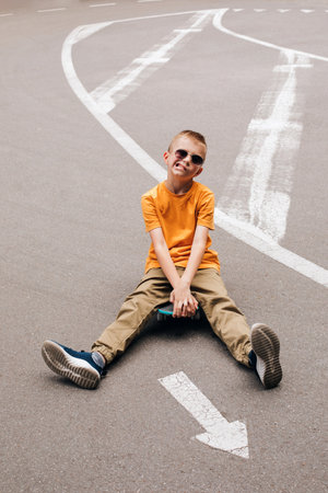 Outdoor activities for children.A cheerful young boy in bright clothes sits on a skateboard. Caucasian schoolboy on a walk. Top viewの写真素材