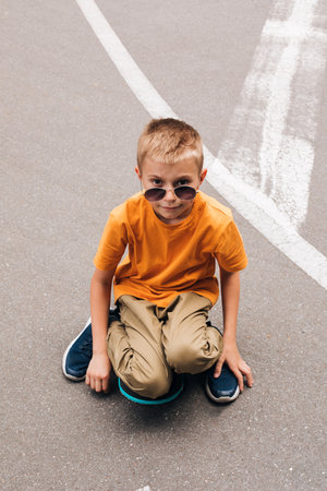 Outdoor activities for children. A cheerful young boy stays on a skateboard on the playground. Caucasian schoolboy on a walk. Front viewの写真素材