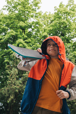 Outdoor activities for children. A cheerful young boy stay with a skateboard in public park....