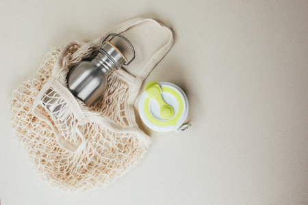 Set of devices for cold and hot drinks. Zero waste concept. A tin bottle for water and a folding mug for coffee with beige mesh bag. Flat layの写真素材