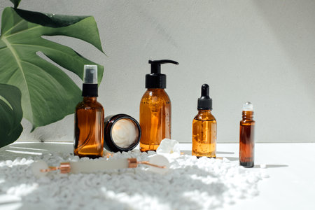 Amber bottles with facial treatment on a yellow table with green leaves on backdrop. Front viewの写真素材