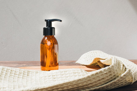 Amber bottle with facial liquid and a green towel on wooden table. Front viewの写真素材