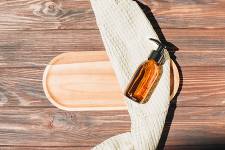Amber bottle with facial liquid and a green towel on wooden table. Flat layの写真素材