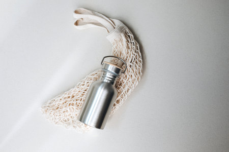 Devices for drinks. Zero waste concept. A tin bottle for water with beige mesh bag on beige background. Flat layの写真素材