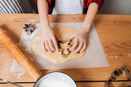 Dad and son at a wooden table in the kitchen making cookies with cookie cutter in a shape of little...