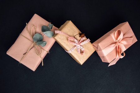 Background for greetings. Gifts wrapping in soft pink paper with dry eucalyptus branch on a black concrete background. Top viewの写真素材