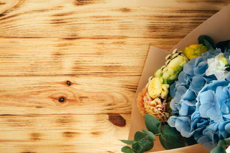 Bouquet of flowers on a wooden background. Floral background, postcard. The bouquet with blue hydrangea and yellow roses is packed in light pink paper. Top viewの写真素材