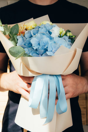 Bouquet of flowers. Floral background, postcard. The bouquet with blue hydrangea and yellow roses wrapped in light pink paper in the hand. Front viewの写真素材