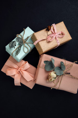 Background for greetings. Gifts wrapping in soft pink paper with dry eucalyptus branch on a black concrete background. Top viewの写真素材