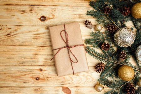 Christmas background for greetings. Gift wrapping in brown paper with branches of coniferous tree, Christmas toys and dry pine cones on a light wooden background. Top viewの写真素材