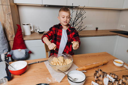 A boy make cookie dough at a wooden table in the kitchen. Cooking desserts at home. Joint activities...