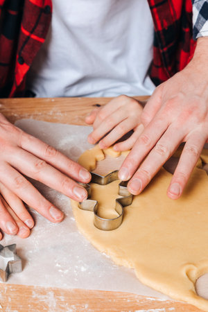 Dad and son at a wooden table in the kitchen making cookies with cookie cutter in a shape of little man. Top viewの写真素材