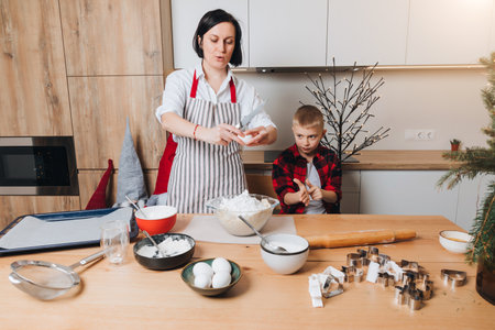 Mom and son are kneading dough for cookies at a wooden table in the kitchen. Cooking desserts at home. Joint activities with children. Front viewの写真素材