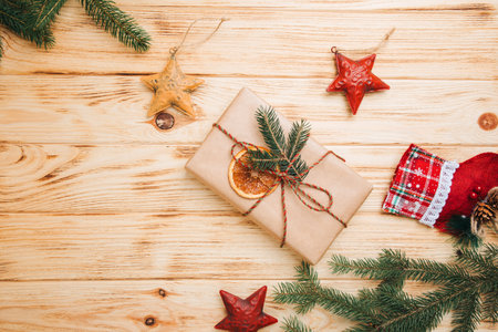 Background for greetings. Gift wrapping in brown paper with dry orange and branch of coniferous tree on a light wooden background. Top viewの写真素材