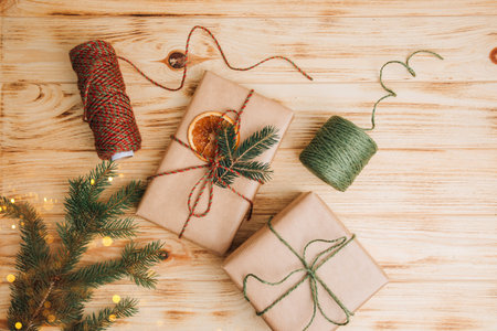 Christmas background. Gift wrapping in brown paper with dry orange and branch of coniferous tree on a light wooden background. The process of packing a Christmas gift. Top viewの写真素材
