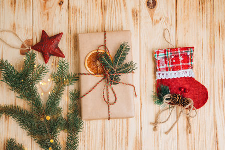 Background for greetings. Gift wrapping in brown paper with dry orange and branch of coniferous tree on a light wooden background. Top viewの写真素材