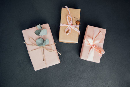 Background for greetings. Gifts wrapping in soft pink paper with dry eucalyptus branch on a black concrete background. Top viewの写真素材