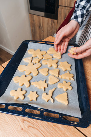 Close up mans hands lay out the formed cookies in the form of a human, stars, Christmas trees on a baking sheet on a wooden table in the kitchen. Cooking desserts at home. Top viewの写真素材