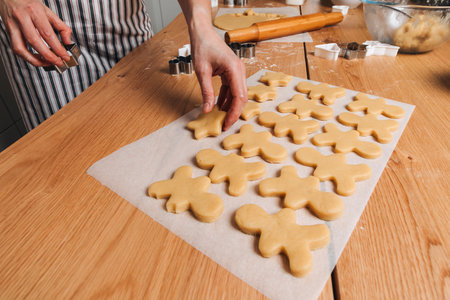 Close up womens hands at a wooden table in the kitchen making cookies with cookie cutter in a shape...