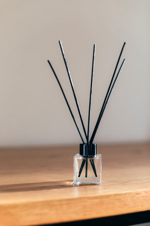 Aroma diffuser in a clear glass bottle with black cap on wooden table on a strip of sunlight. Front...
