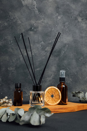 Aroma diffuser in a clear glass bottle with black cap and spray bottle on wooden tray on a dark...
