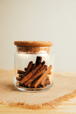 A cinnamon stick in glass jar on a light wooden background. Spices, herbs. Front view, selective focusの写真素材