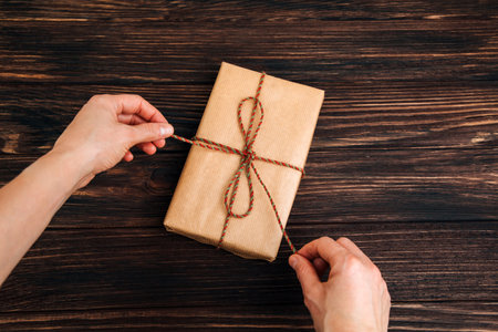Christmas, festive background. Gifts wrapping in brown paper in womens hand on a dark wooden...