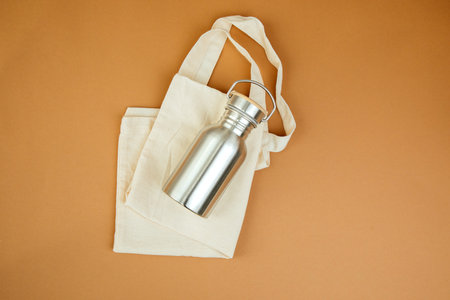 Devices for drinks. Zero waste concept. A tin bottle for water with beige bag on a brown background. Flat layの写真素材