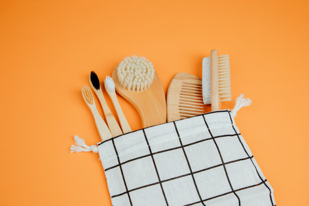 Set eco friendly bath devices. Wooden brushes, comb, bamboo toothbrushes in textile bag on an orange...