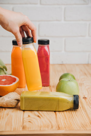 Fruit and vegetable smoothies in transparent plastic bottles. Red, green, orange smoothies on a wooden table with womens hand. The concept of healthy eating. Front viewの写真素材
